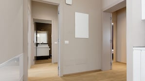 A modern, minimalist hallway with wooden flooring and white walls, leading to a kitchen area with a countertop and cabinets. - MyPlace - Appartamento Family Deluxe Terrace (Treviso)