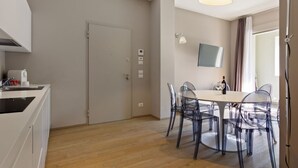 A modern kitchen with a white countertop and a dining area with transparent chairs and a round table. - MyPlace - Appartamento Family Deluxe Terrace (Treviso)