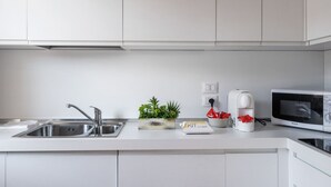 Une cuisine moderne équipée d’un évier en acier inoxydable, d’un four à micro-ondes et d’une machine à café. On peut voir une petite plante sur le plan de travail et une boîte étiquetée « ZKTP ».