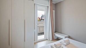 Une chambre d’hôtel avec un lit, une banquette, une armoire et un balcon donnant sur des immeubles.