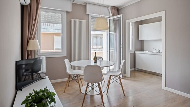 Un salon moderne doté d’un téléviseur à écran plat, d’une table à manger avec des chaises, d’une plante en pot et d’une grande fenêtre avec des rideaux.