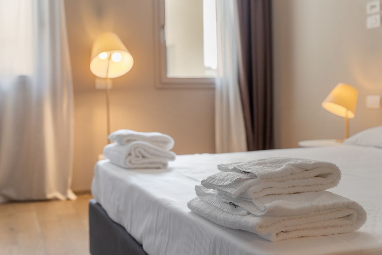 Uma cama bem arrumada com toalhas brancas dobradas e duas luminárias de piso que oferecem iluminação suave.