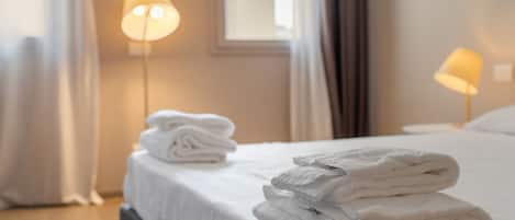 A neatly made bed with folded white towels and two floor lamps providing soft lighting.