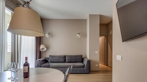 Een moderne woonkamer met een ronde eettafel, een bank en een aan de muur bevestigde televisie.