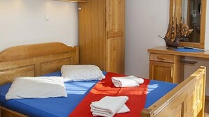 A single bed with a blue mattress and a red blanket, wooden headboard, and a wooden wardrobe with open doors. - Lovely studio for 2 persons (Makarska)