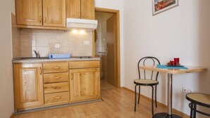 A kitchen with wooden cabinets, a countertop, and a small dining area with two chairs and a table. - Lovely studio for 2 persons (Makarska)