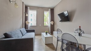 A modern living room with a grey sofa, a white coffee table, a dining table with chairs, and a flat-screen TV mounted on the wall. - MyPlace Piazza Vittoria Apartment (Treviso)