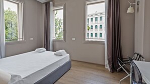 A hotel room with a bed, a table, and two windows. - MyPlace Piazza Vittoria Apartment (Treviso)