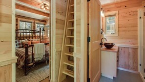Ein gemütliches Blockhaus-Interieur mit Bett, einer Leiter, einem Waschbecken und einem Fenster.