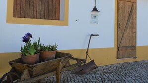 Ein Gebäude mit einer Holztür, einem Fenster mit Holzklappläden, einer Wandleuchte und einem Rasenwagen mit Blumentöpfen.
