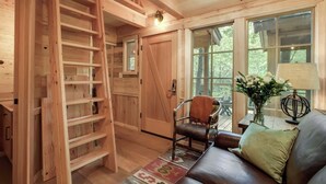 Una habitación acogedora con una escalera de madera, un sofá de cuero, una silla y una mesa con una lámpara y flores.