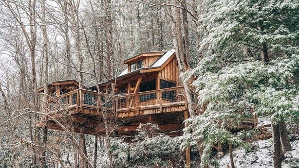 Una casa del árbol de madera con varios niveles y balcones, rodeada por un bosque nevado.