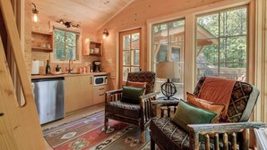 Accogliente interno di una baita con arredamento in legno, una cucina con frigorifero, microonde e macchina del caffè, e un angolo salotto con tappeto decorato.