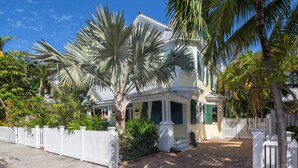 A two-story house with a porch, surrounded by a white picket fence and various tropical plants. - SUNCATCHER~4 Bedroom, 4 Bathroom in Old Town with Pool! (Key West)
