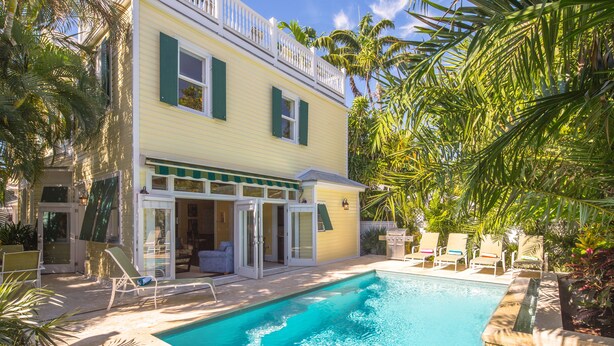 A yellow building with a pool, outdoor seating, and palm trees. - SUNCATCHER~4 Bedroom, 4 Bathroom in Old Town with Pool! (Key West)
