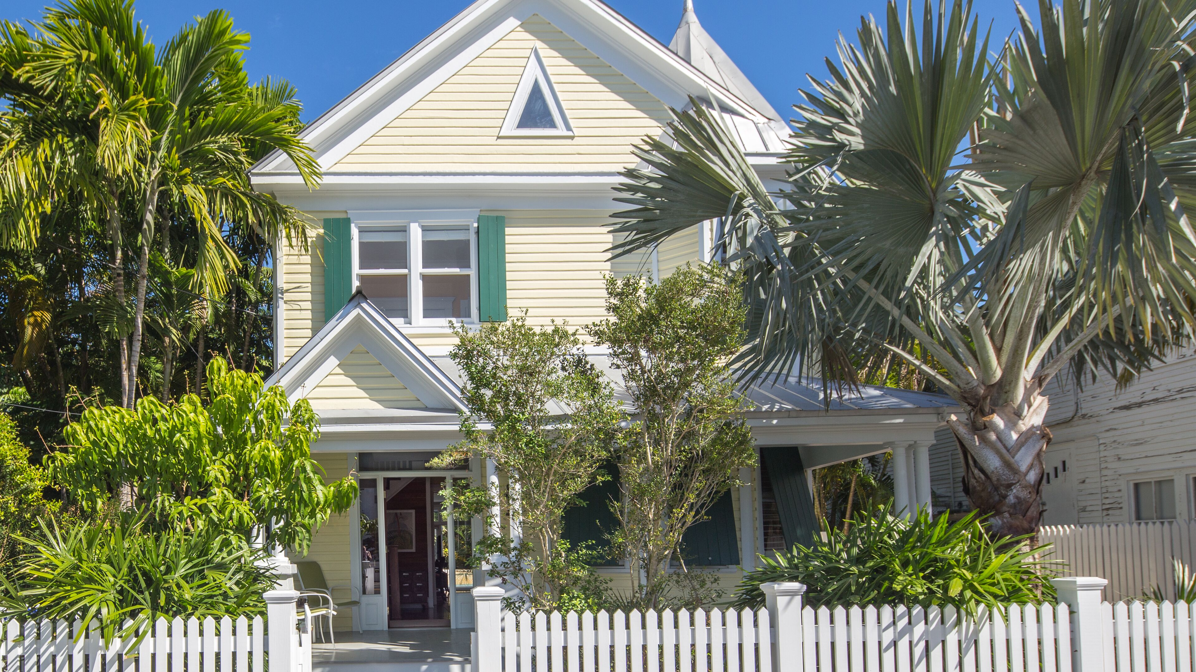 A two-story house with a white picket fence, green shutters, and a small porch.