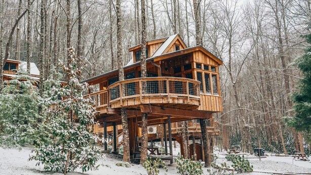Una cabaña de madera con varios niveles, rodeada por un bosque nevado.