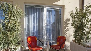 A small patio with two red chairs and a glass table, surrounded by potted plants and a sliding glass door. - Apartment Almera N2 (Makarska)