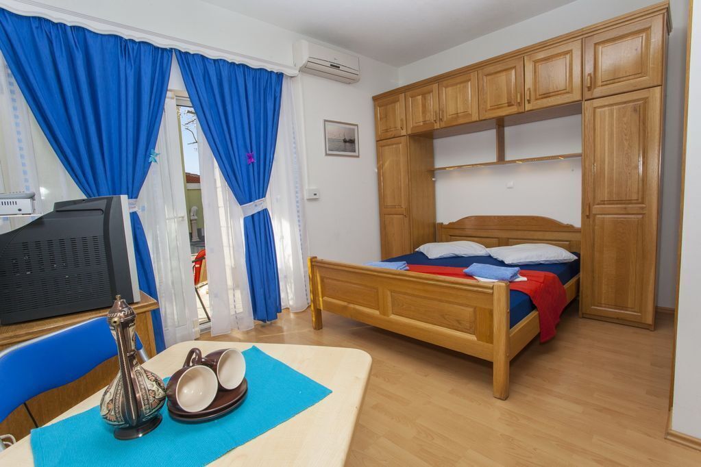 A room with a bed, wooden cabinets, a television, and a table with a decorative item and cups.