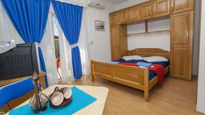 Quarto com cama, armários de madeira, televisão e mesa com objeto decorativo e xícaras.