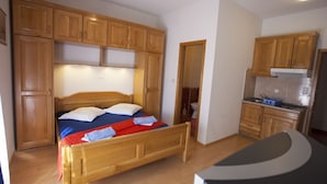 Quarto compacto com cama de madeira, pequena cozinha e armários de madeira.