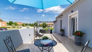 Un espacio al aire libre techado con mesa y sillas, una silla colgante y plantas en macetas.