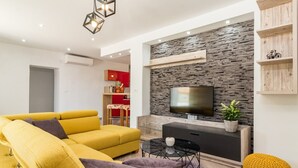 Una sala de estar moderna con un sofá amarillo, una mesa de centro negra y un televisor de pantalla plana montado en una pared de piedra.