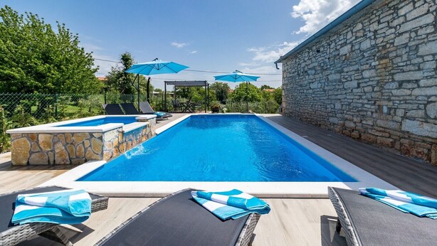 Una piscina con tumbonas y sombrillas, rodeada de muros de piedra y vegetación.