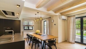 A modern kitchen with a central island, black chairs, pendant lighting, and a view of the outdoors through large windows. - Modernly designed villa located near Pula (Manjadvorci)