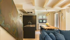 A modern kitchen with a central island, a dining area with a wooden table and chairs, and a blue sofa in a living area. - Modernly designed villa located near Pula (Manjadvorci)