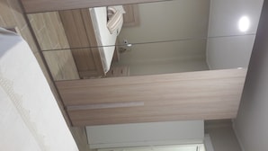 A modern hotel room with a large mirror, wooden flooring, and a white bed.
