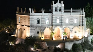 A large, historic building with multiple arches and a central tower, illuminated at night.