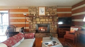 Un salon chaleureux avec une cheminée en pierre, un téléviseur et un canapé agrémenté de coussins rouges.