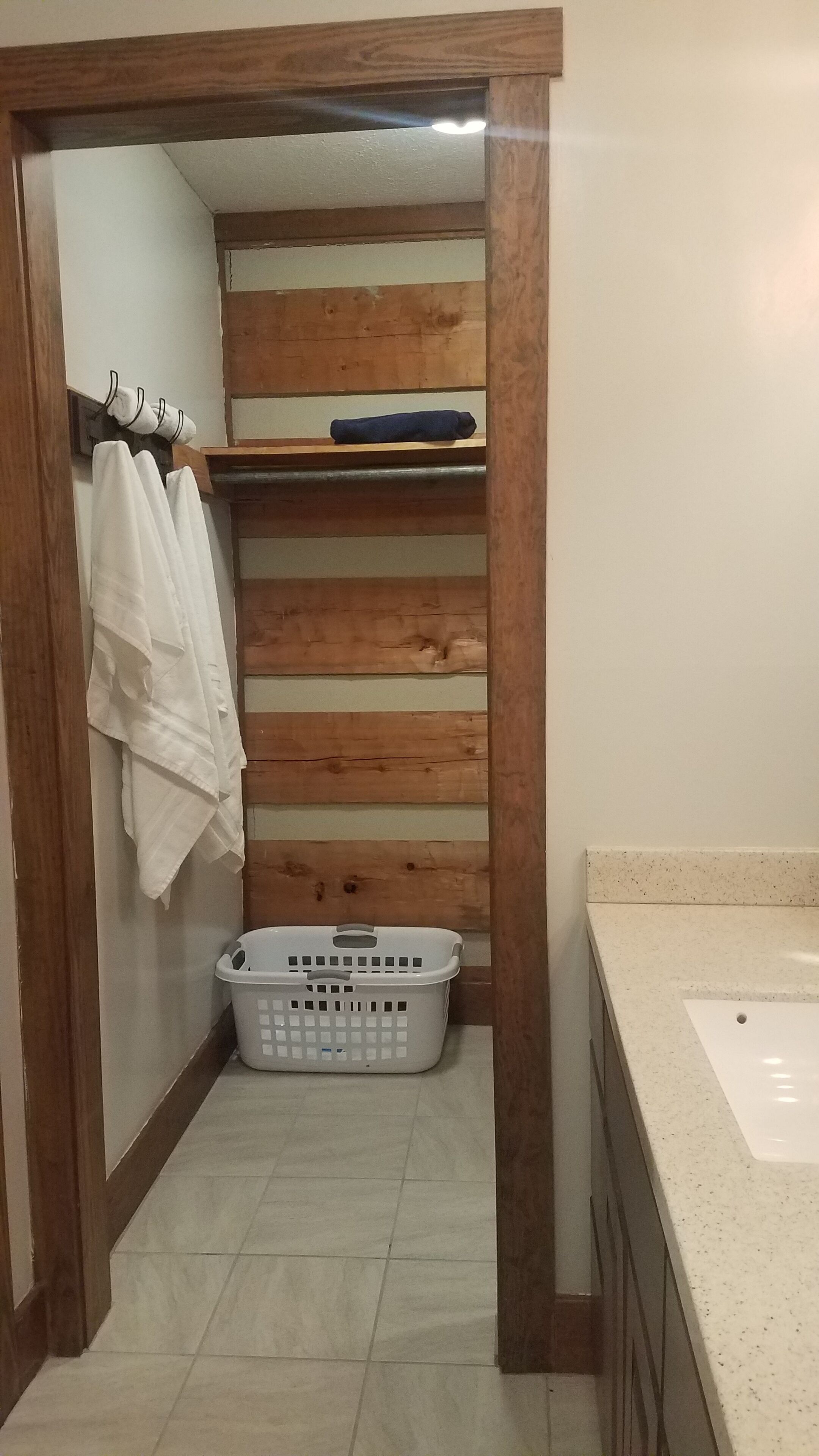 Un baño con un estante de madera, un cesto de ropa blanca y una bañera.