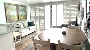 Un comedor moderno con una mesa redonda de madera, sillas blancas tapizadas y un sofá de tonos claros.
