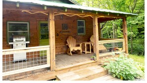 Eine Holzhütte mit Veranda, Grill und Adirondack-Stühlen.