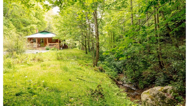 Eine Hütte in bewaldeter Landschaft mit Veranda und einem kleinen Bach in der Nähe.