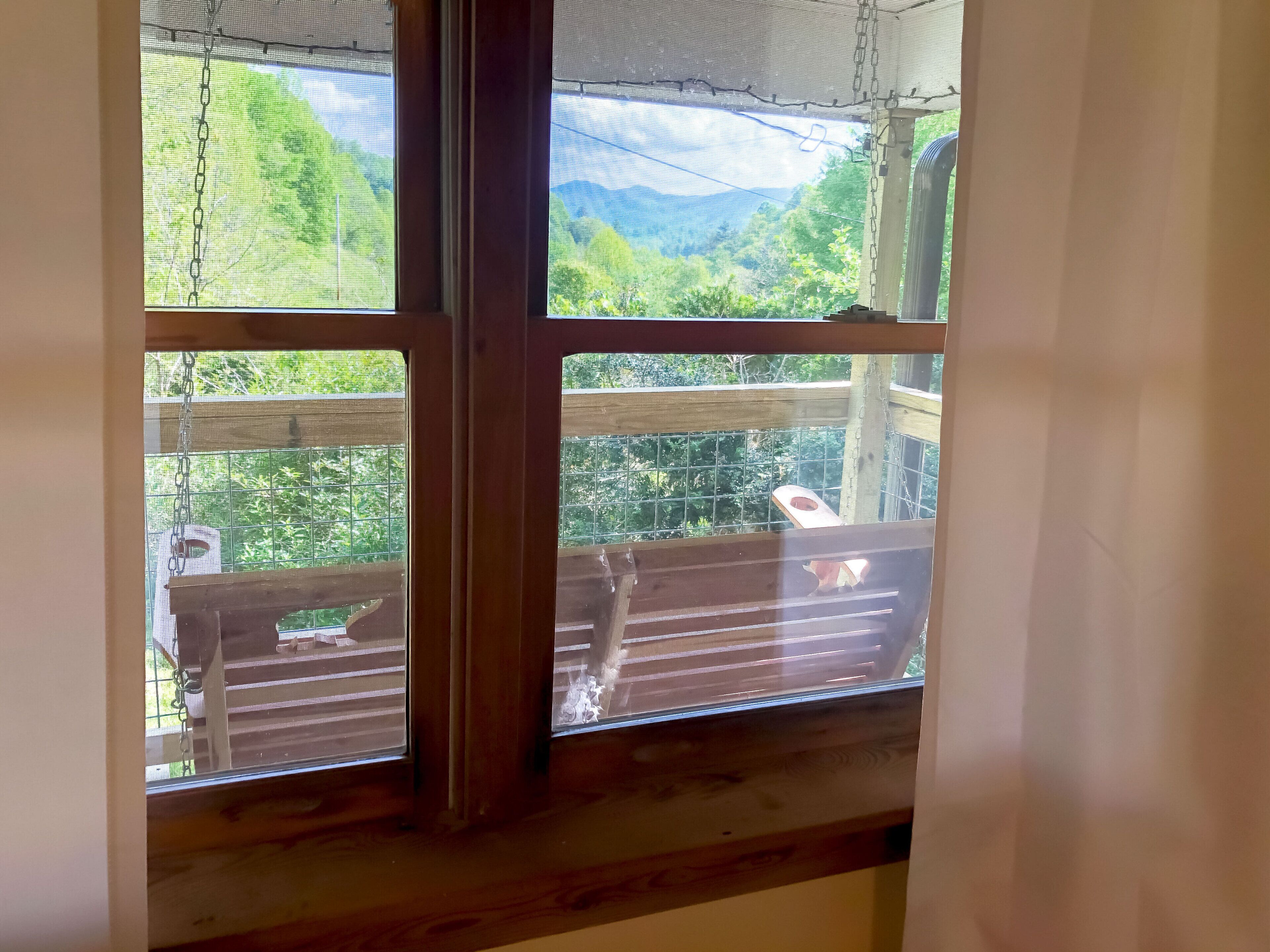 A window with a view of a wooden deck and a fenced area with greenery.
