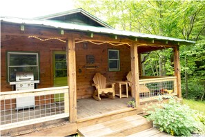 A wooden cabin with a porch, a grill, and Adirondack chairs.