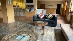 Un hall d’hôtel avec un comptoir d’accueil, un canapé bleu orné de coussins à rayures et une table basse ronde en bois.