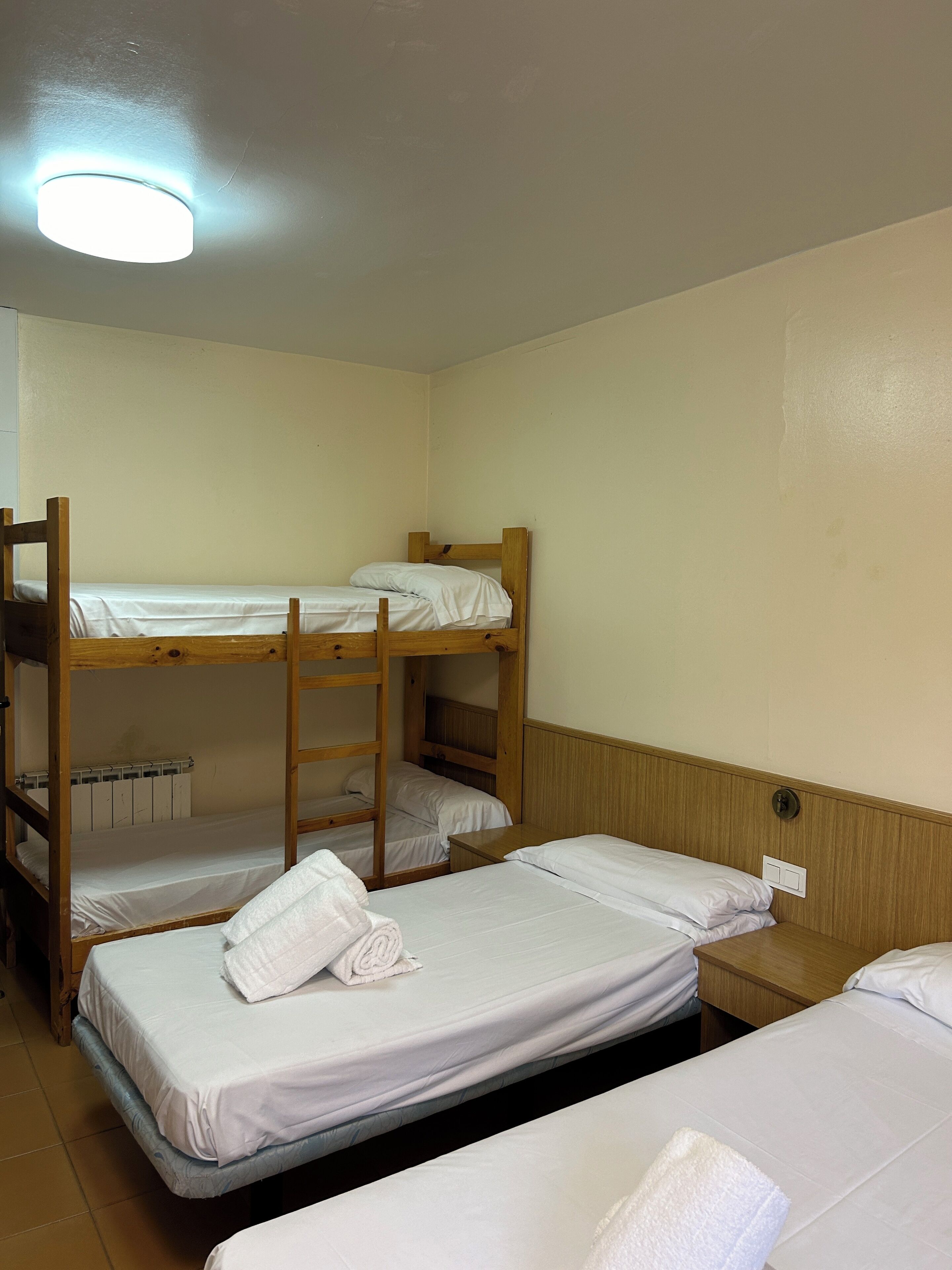 Ein Schlafsaalzimmer mit Etagenbetten, einem Holz-Kopfteil, einem kleinen Nachttisch und einer Wandleuchte.