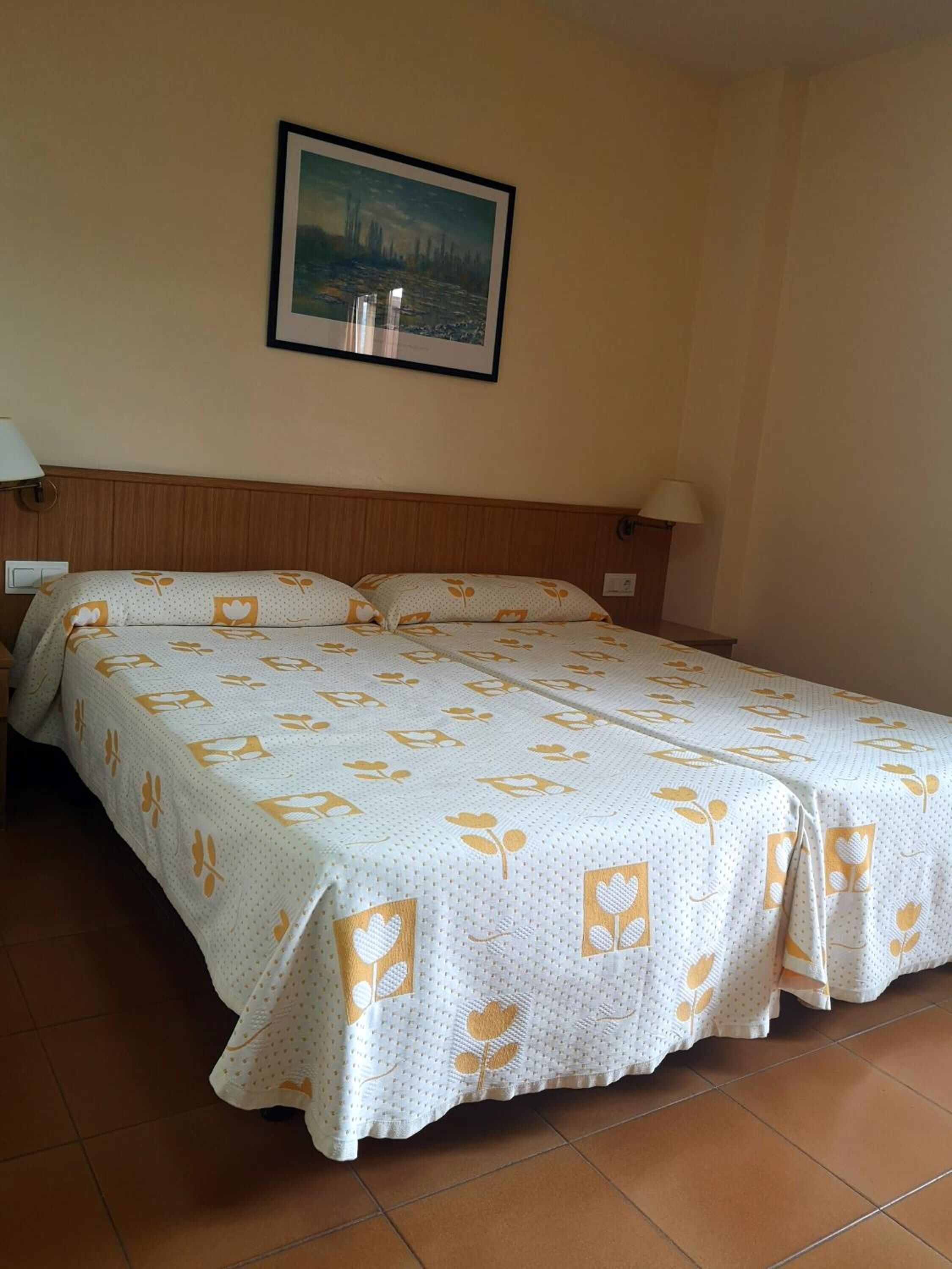 Ein Doppelbett mit floralem Überwurf, zwei Nachttischlampen, ein gerahmtes Bild an der Wand und ein hölzernes Kopfteil.