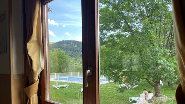 Une pièce dotée d’une grande fenêtre donnant sur une piscine et un espace verdoyant avec des arbres.