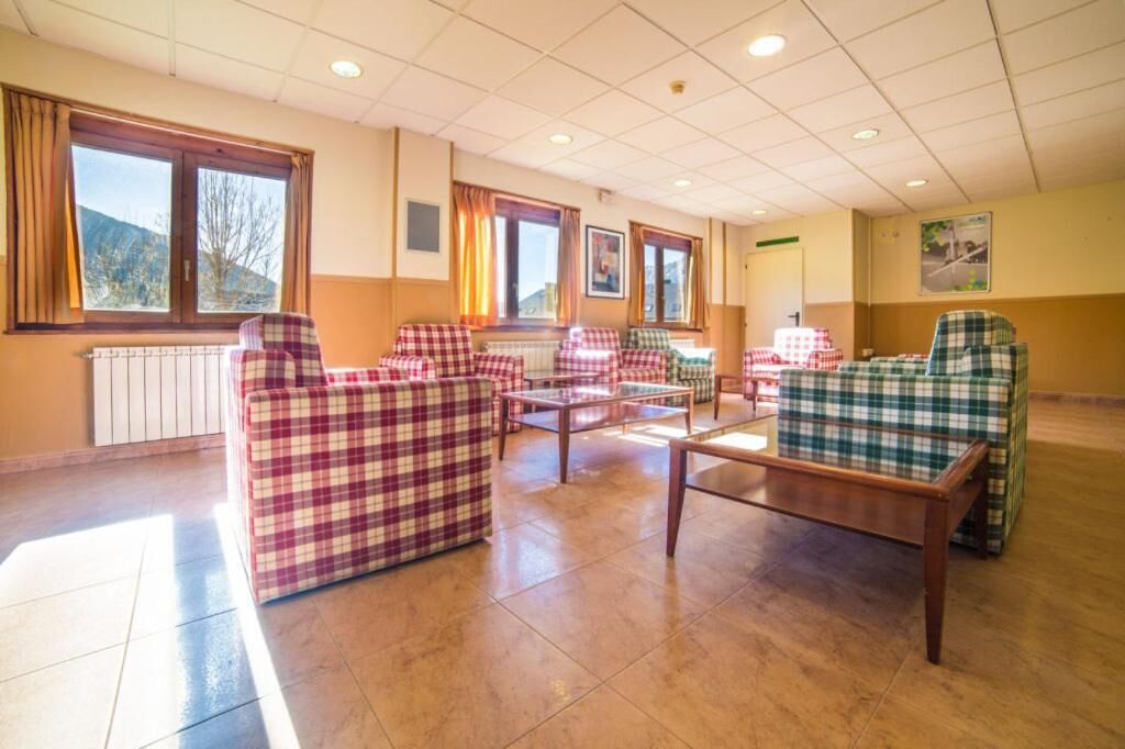A spacious room with checkered sofas and tables, large windows with curtains, and a radiator on the wall.