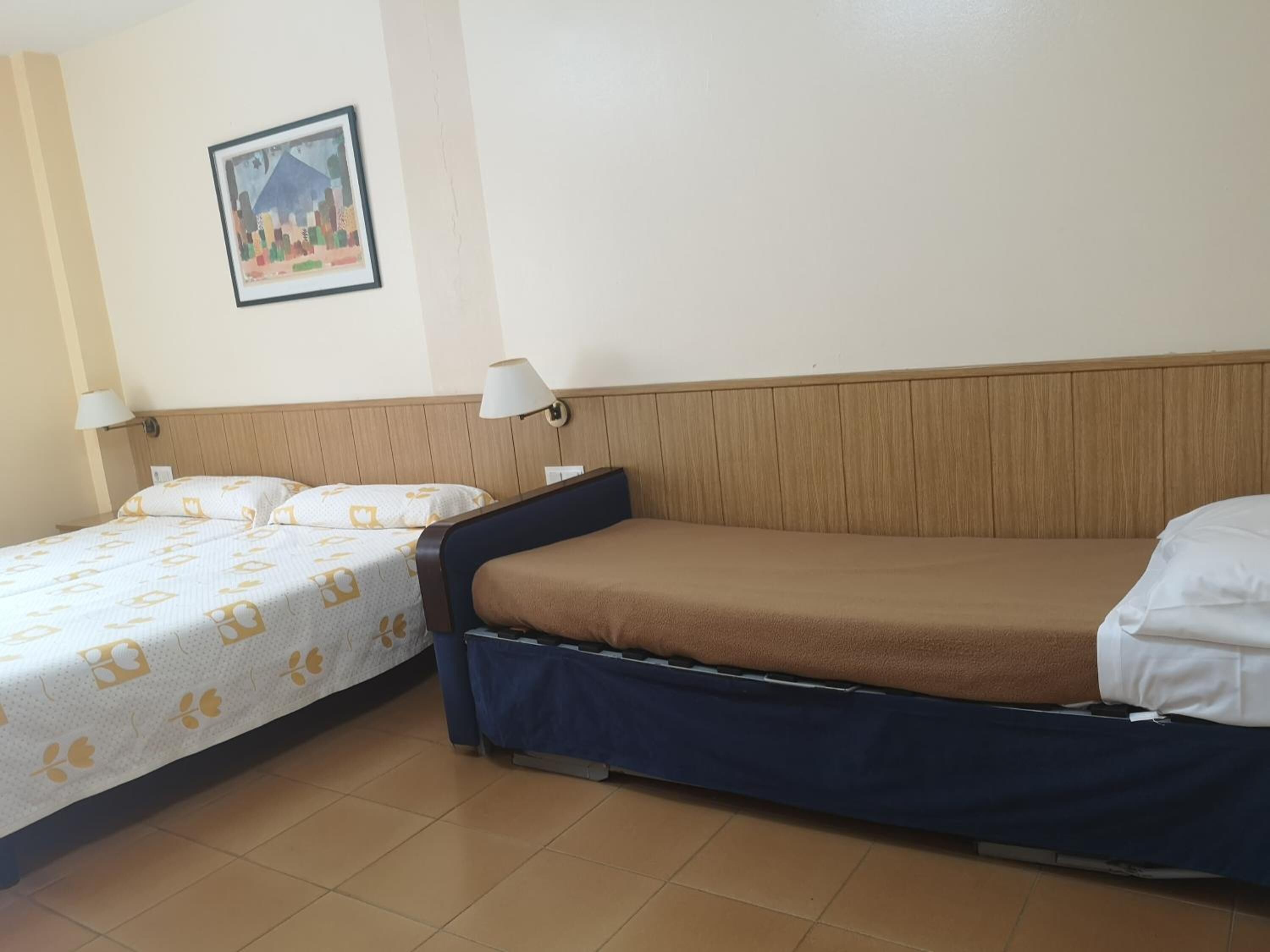 A hotel room with two beds, a wooden headboard, a wall-mounted lamp, and a framed picture.
