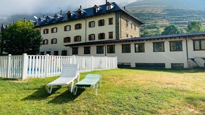 Un hôtel à plusieurs étages, avec une clôture blanche et un espace piscine équipé de chaises longues.