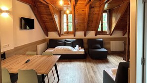Una habitación estilo loft acogedora, con techo de madera, una mesa de comedor con sillas, un sofá y un televisor montado en la pared.