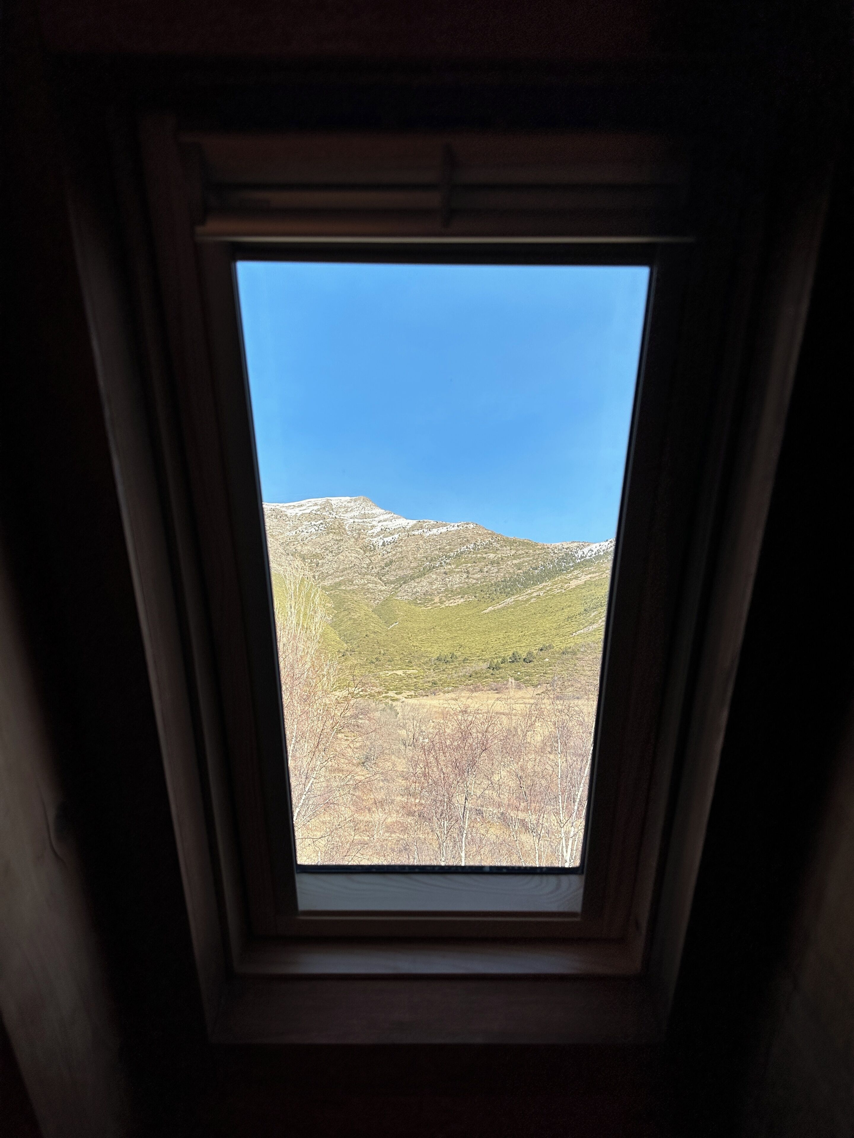 Een dakraam met uitzicht op een bergachtig landschap.