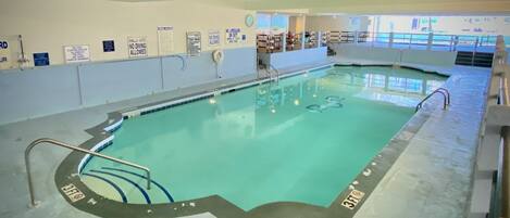 Una piscina interior con agua cristalina, zonas de profundidad señalizadas y señales de seguridad en las paredes.