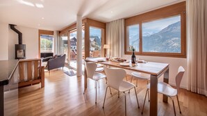 Un interior moderno con una mesa de comedor de madera, sillas blancas y grandes ventanales con vistas a la montaña.